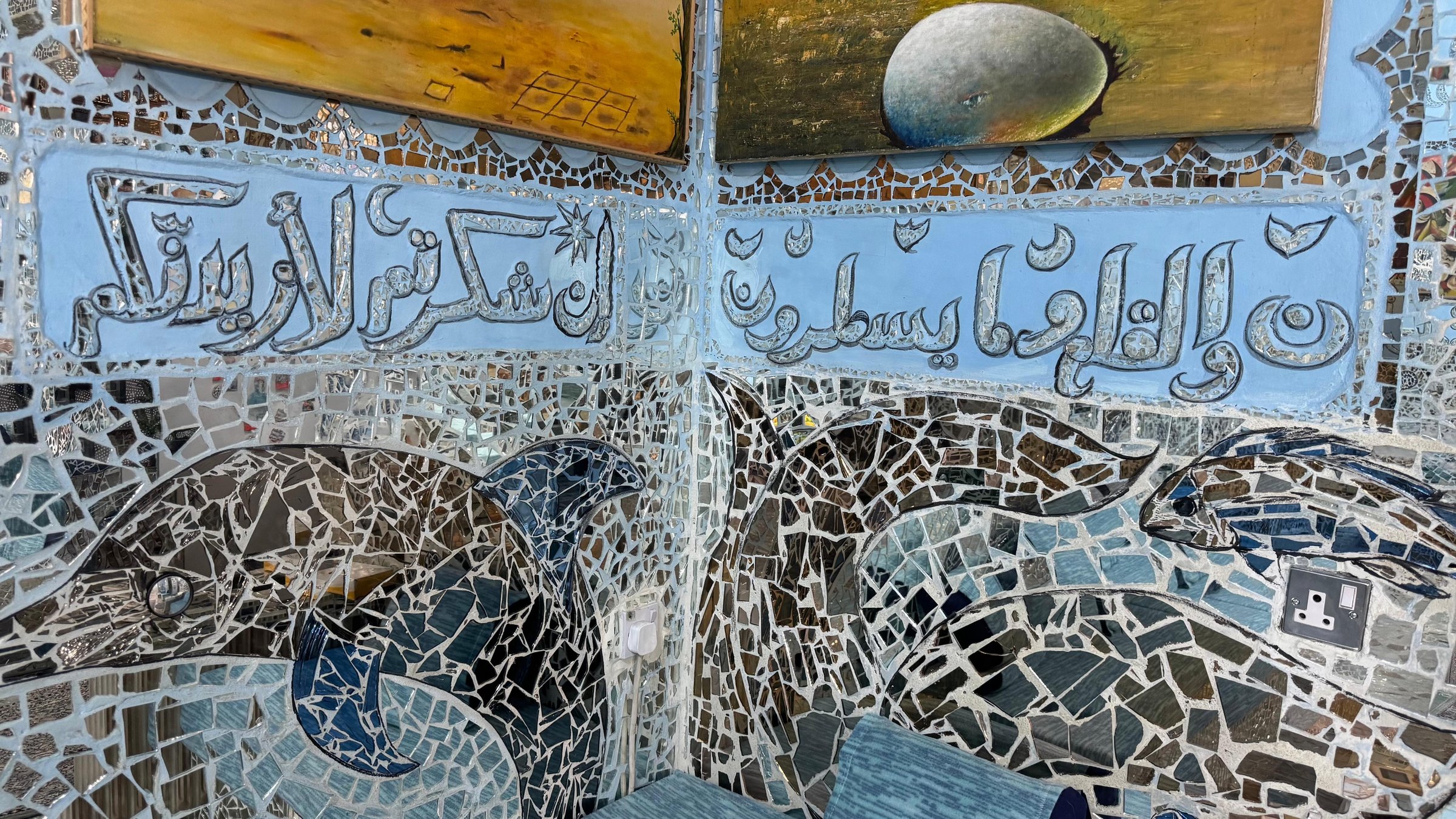 Mirror-mosaic dolphins beneath a band of calligraphy in the Sea World Hall