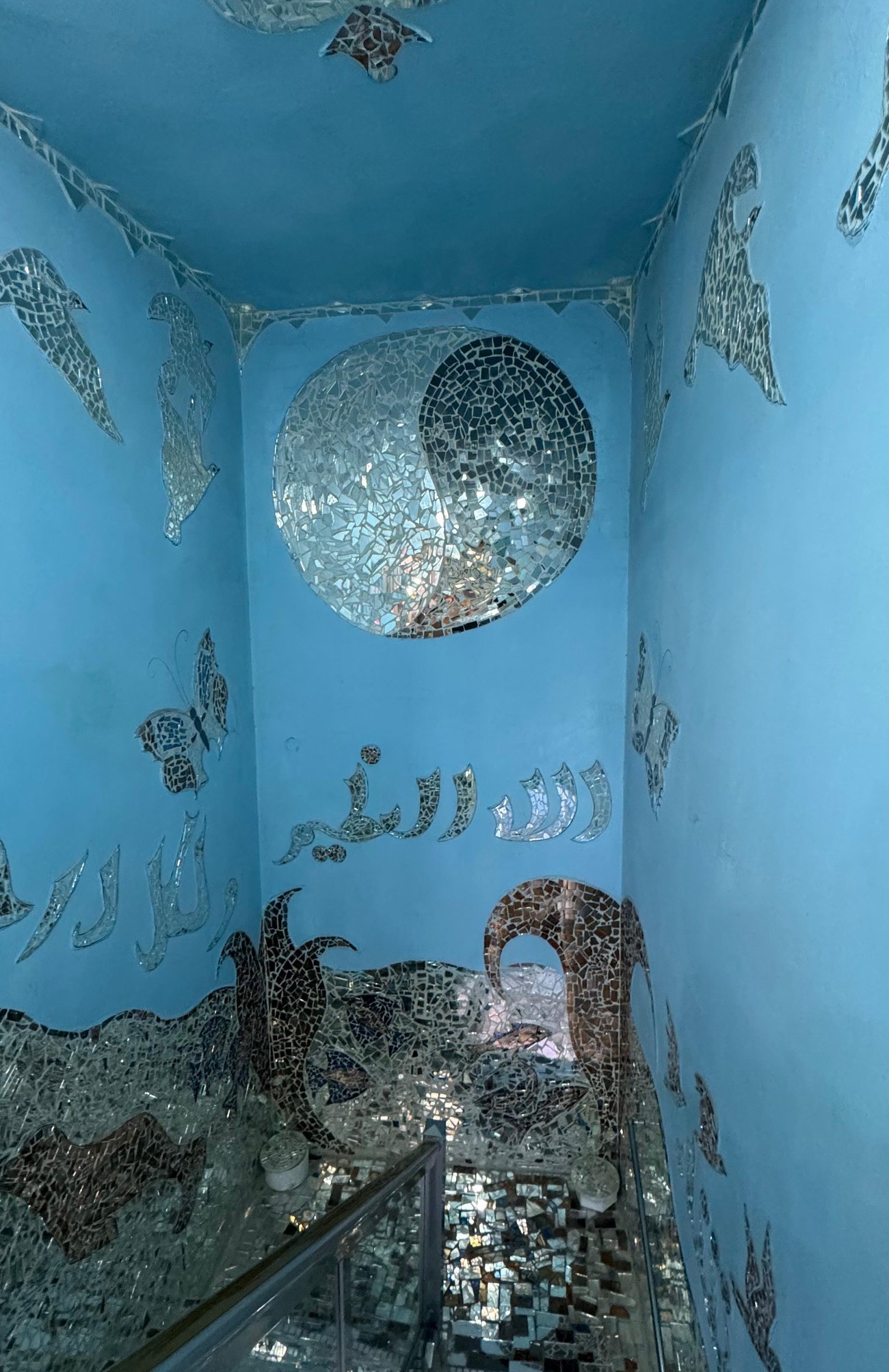 A blue stairwell beneath a circular mirror medallion, above waves and calligraphy